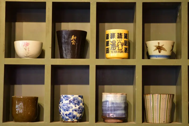 An array of decorative ceramic cups displayed in wooden cubby shelves with artistic designs