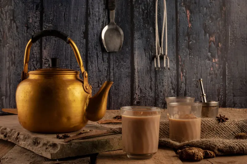 Charming setup featuring a brass kettle and glasses of Indian chai on a rustic table