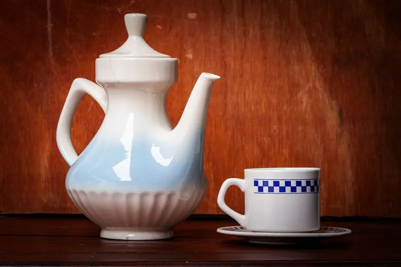 A ceramic teapot with a matching cup on a wooden surface, showcasing classic tableware style
