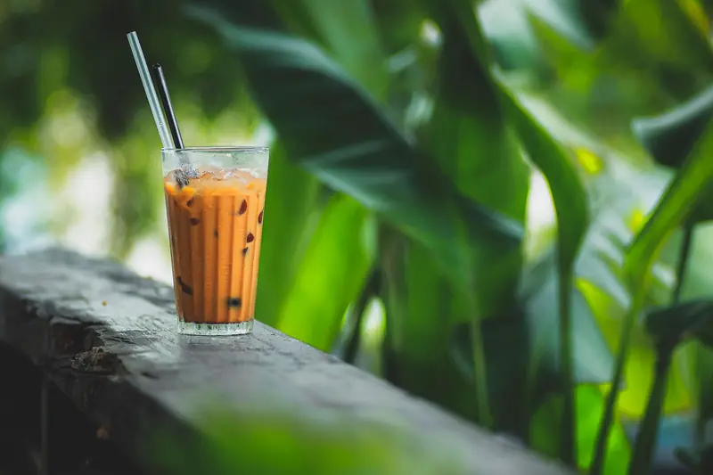 Glass of iced tea with straw on a rustic table amidst lush green foliage