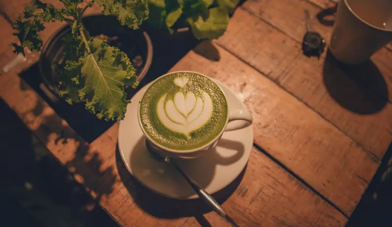 A warm indoor scene of a matcha latte with beautiful latte art on a rustic wooden table