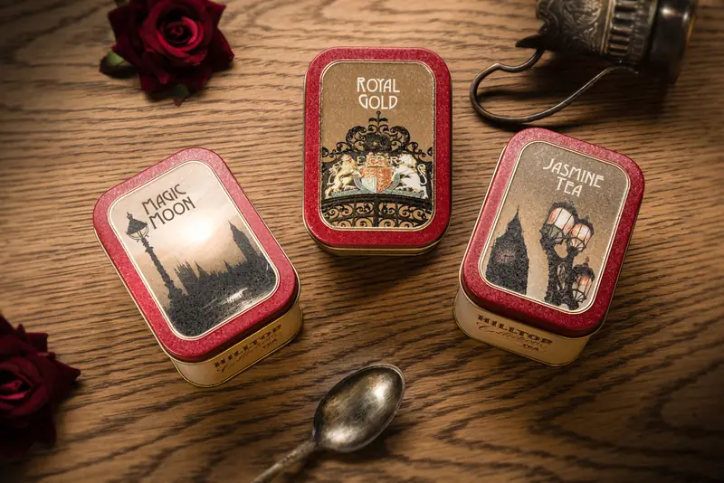 Top view of three elegant tea tins with labels, accompanied by a vintage spoon, on a wooden surface
