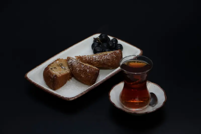 A delicious arrangement of sliced cake, black grapes, and tea on a dark background, creating a cozy vibe