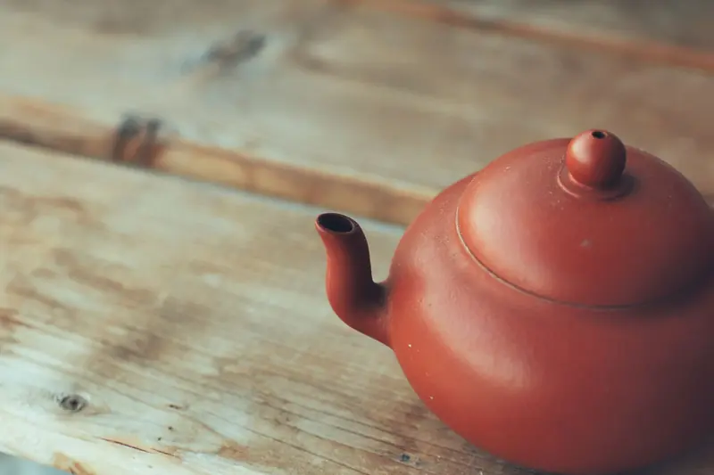 A close-up of a red clay teapot placed on a rustic wooden table with soft lighting