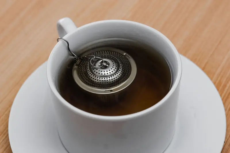 A close-up view of a tea infuser steeping in a white cup of tea on a wooden table