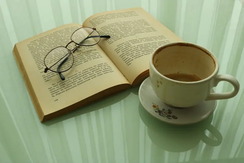 Open book with glasses and used coffee cup on a reflective surface, ideal for literature lovers
