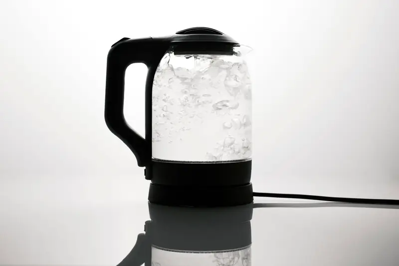 A sleek electric kettle boiling water, captured on a reflective white surface