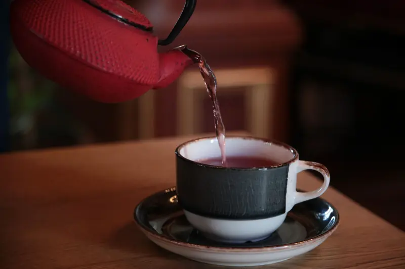 Red kettle pouring tea into a stylish cup on a wooden table, creating a cozy atmosphere indoors