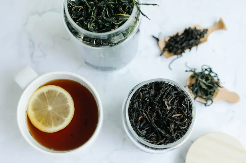 Close-up shot of a cup of tea with a lemon slice and jars of loose leaf tea on a marble surface