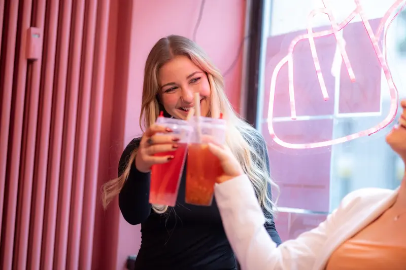 Two women smiling while toasting bubble tea in a vibrant indoor setting