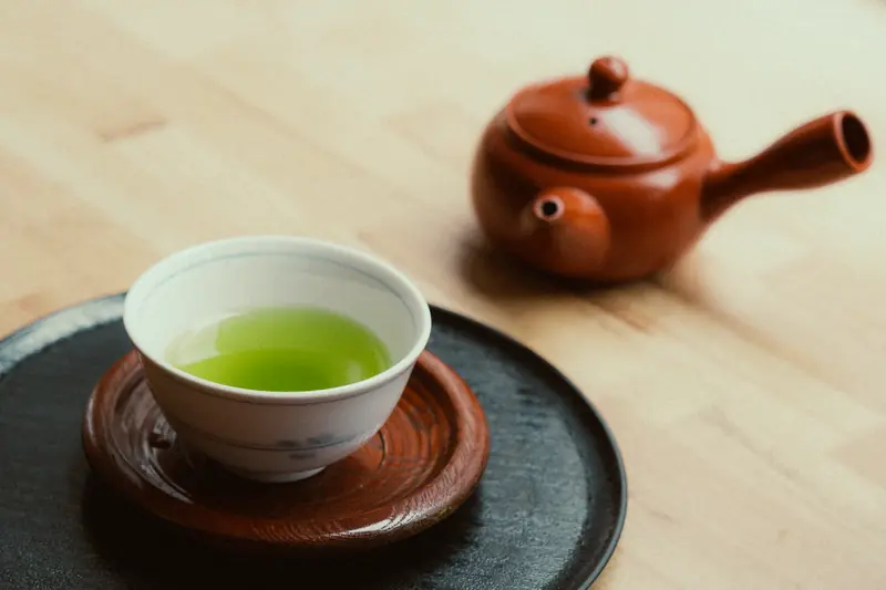 A cup of vibrant green tea and a clay teapot on wooden surface, capturing a calming essence