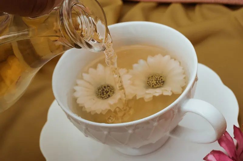 Close-up of herbal tea being poured into a white teacup with floating flowers, creating a serene and relaxing scene
