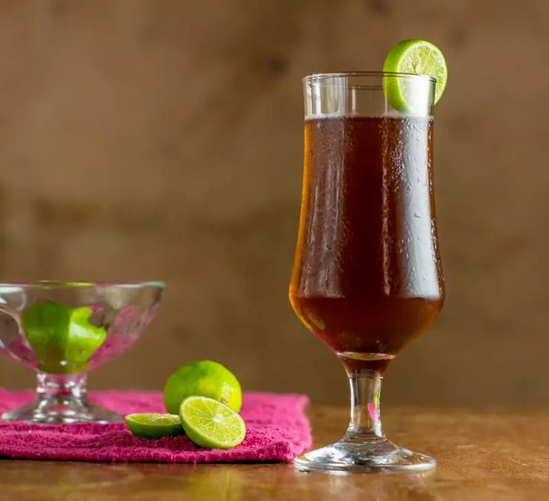 A tall glass of iced tea garnished with a lime slice, placed on a wooden table with a pink fabric underlime