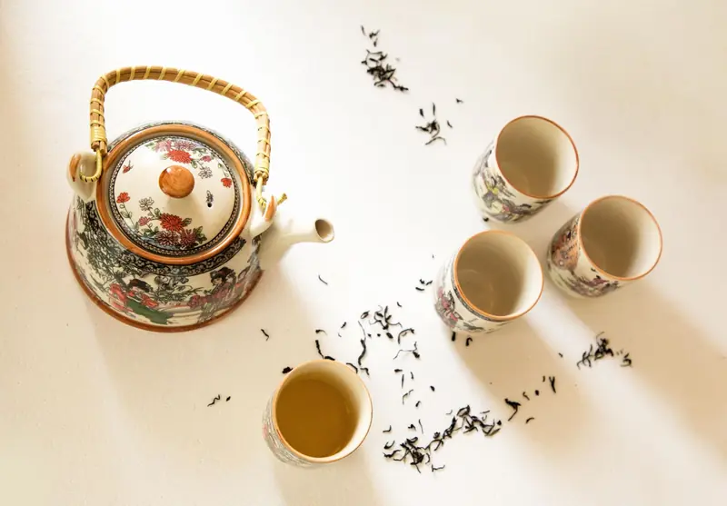 Beautifully designed teapot and cups with loose leaf tea on a light surface, creating a serene tea setting