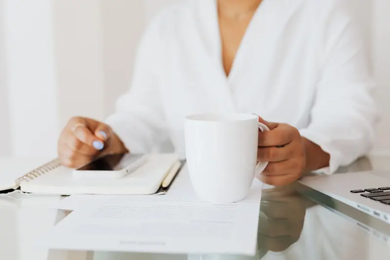 Woman holding a white mug at a desk with documents and laptop in an office