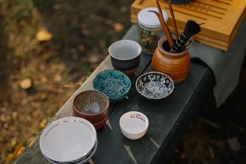 An assortment of rustic tea cups and bowls on a wooden table outdoors, capturing a serene setting
